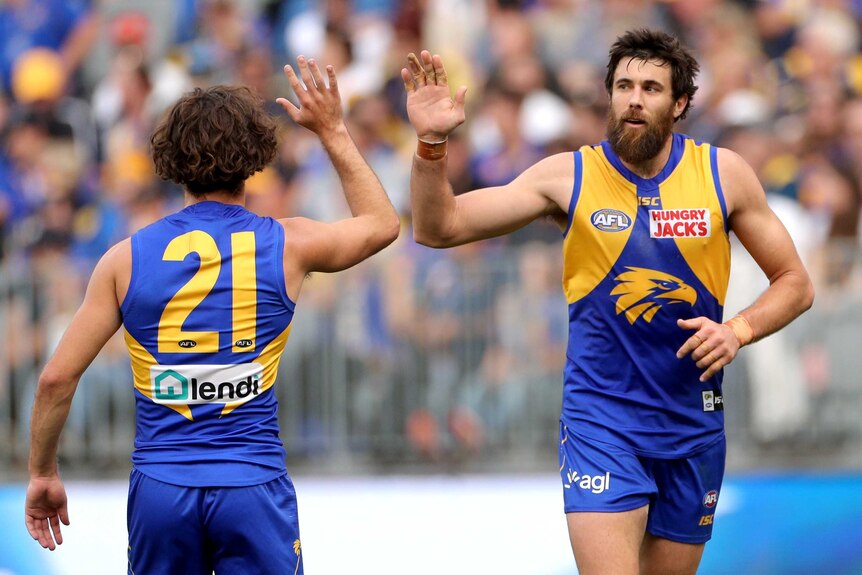 A male AFL player runs and gives a high five to a teammate going in the opposition direction.