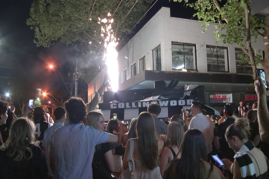 Crowds gather around a van that has Collingwood written on its roof as a flare is set off in the background.