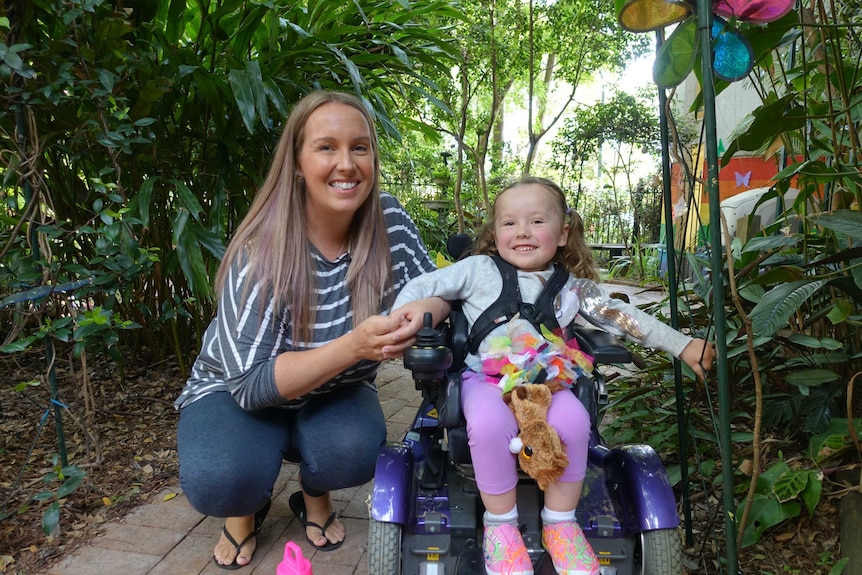 Hayley bends down next to Ruby who is in a mobility scooter.