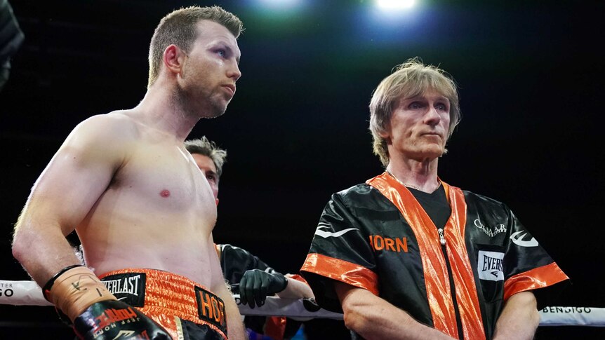 A boxer stands next to his trainer as they wait for the start of a fight.