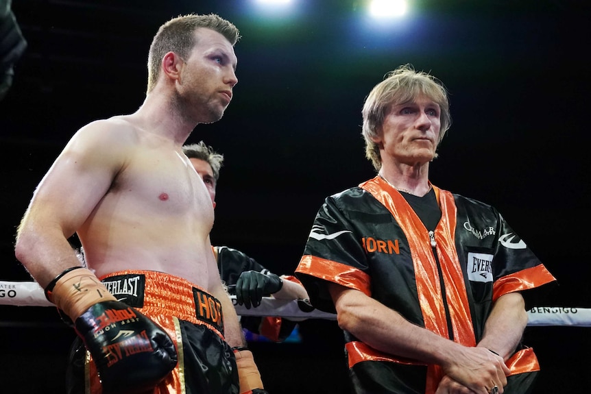 A boxer stands next to his trainer as they wait for the start of a fight.