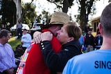 A woman, with her face visible, hugs a man wearing a straw hat and red top.