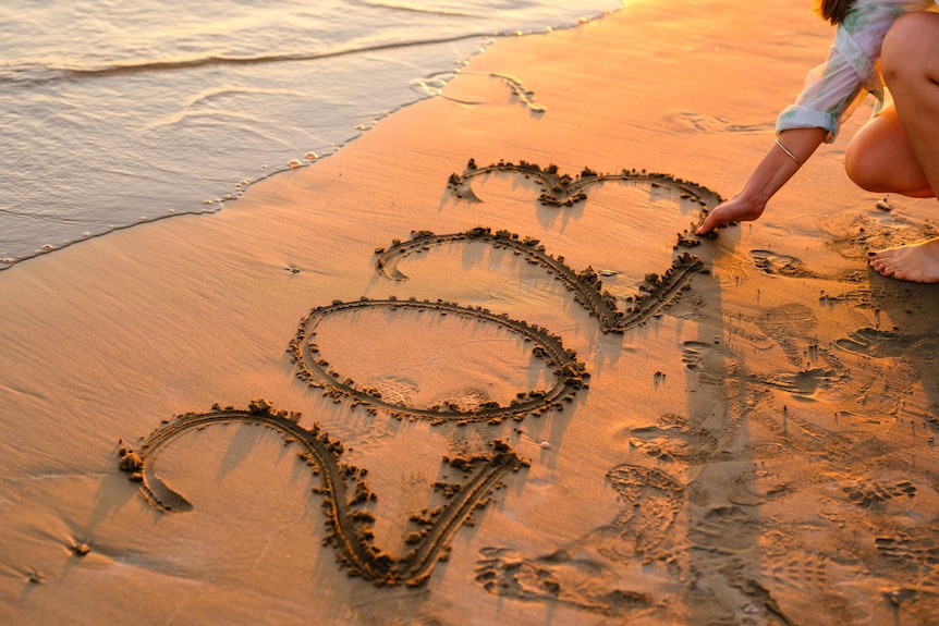 A woman writing 2023 in the sand at the beach during sunset