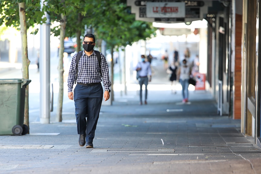 A man wearing a mask walking down a Perth street