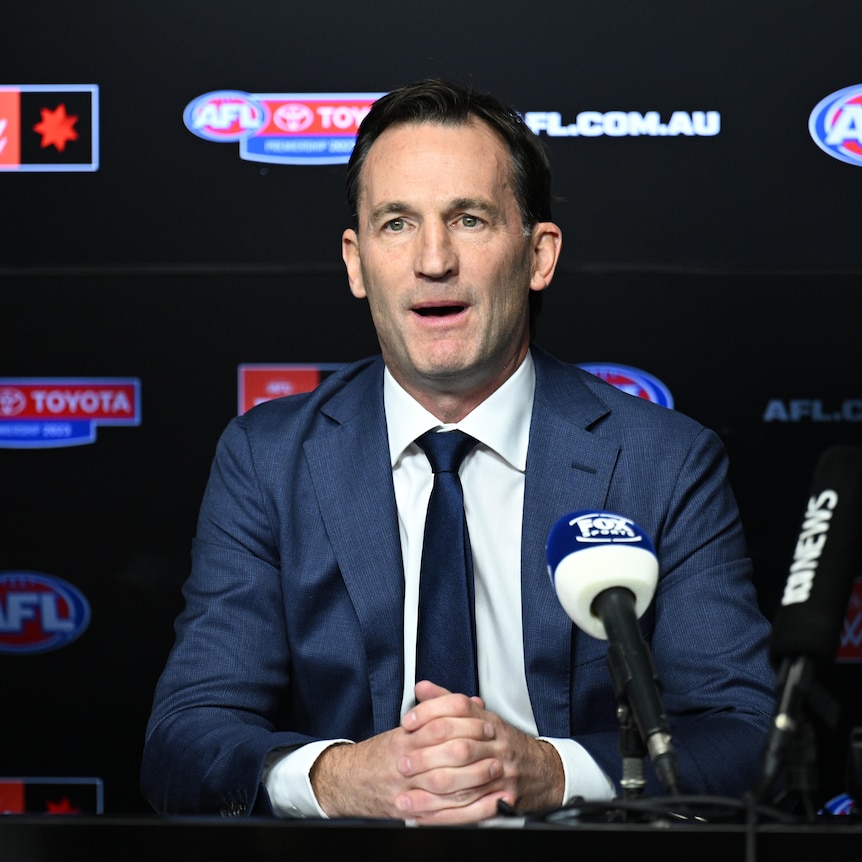 A top AFL executive sits at a desk facing the media with microphones in front of him.