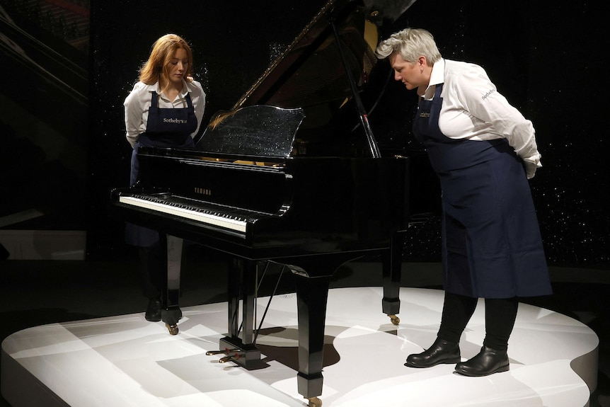 two people in aprons look at a black baby grand piano