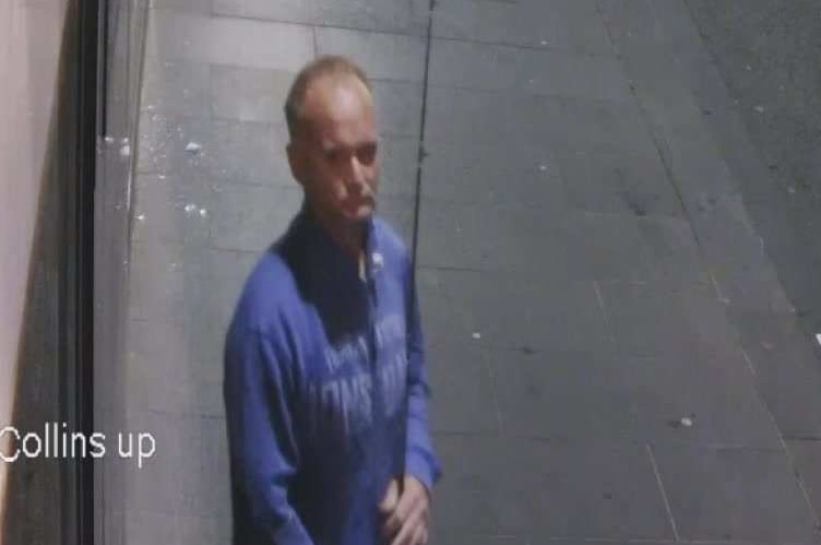 A man in a blue jumper holds a fishing rod in a street at night.