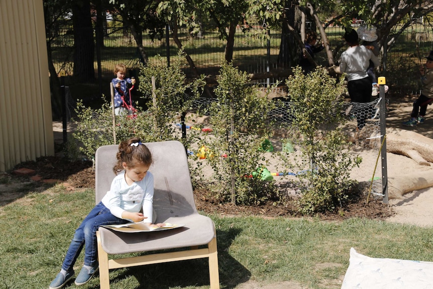 Young girl sitting in a chair reading a book in a preschool playground