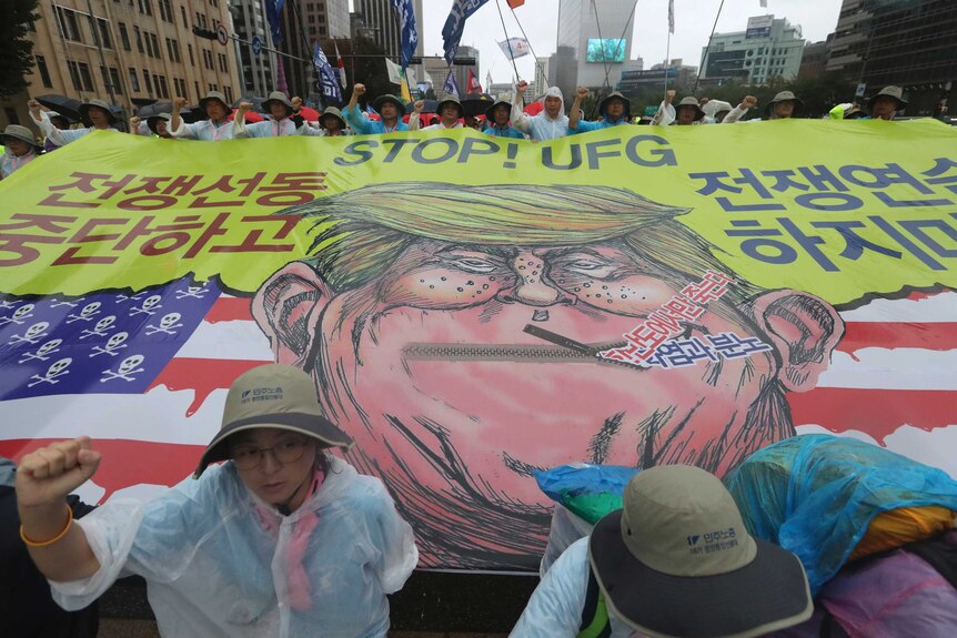 Protesters march behind a giant banner emblazoned with a caricature of Donald Trump.