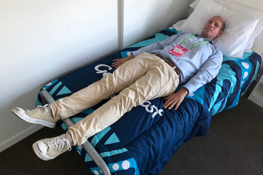 ABC reporter Tom Forbes tries out a bed in the Commonwealth Games Athlete's Village.