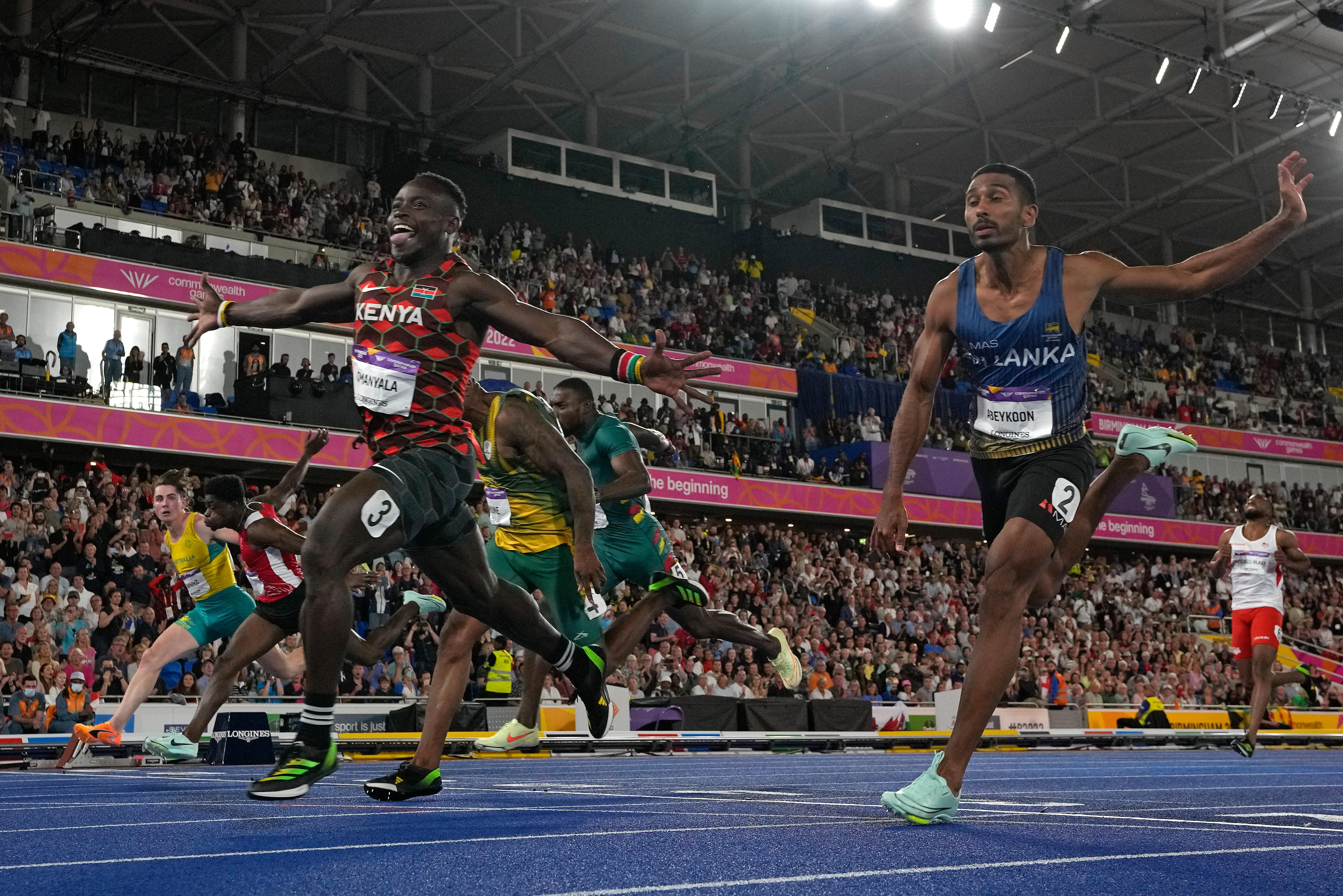 kenyan runner crosses 100m sprint finish line with arms outstretched and poking tongue out with big smile