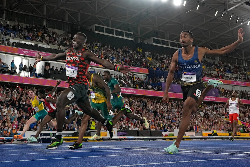 kenyan runner crosses 100m sprint finish line with arms outstretched and poking tongue out with big smile