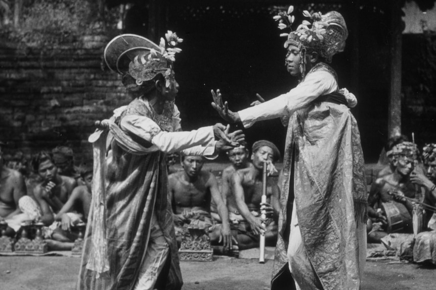 Two dancers in traditional Balinese costume face each other, with a gamelan gumbuh ensemble in Bali.