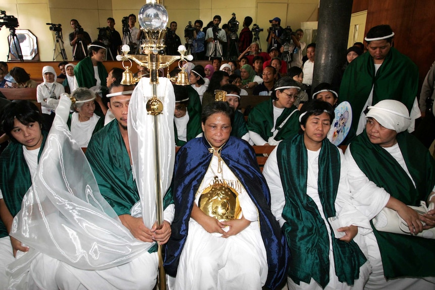 A woman wearing white and a blue robe in court surrounded by her supporters, wearing white with a green shawl.