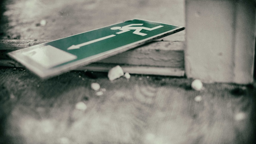 An green emergency exit sign slays discarded on a grey concrete floor