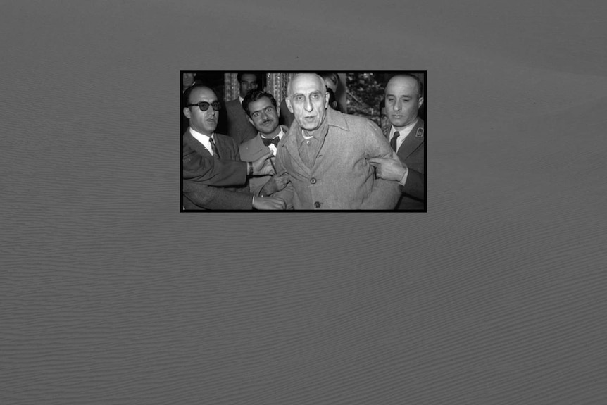 Men in suits grip Mohammad Mossadeq by the arms