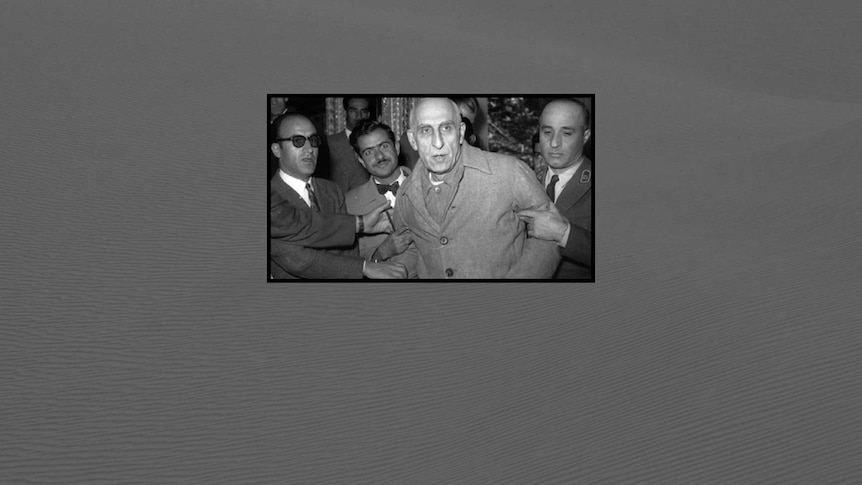 Men in suits grip Mohammad Mossadeq by the arms