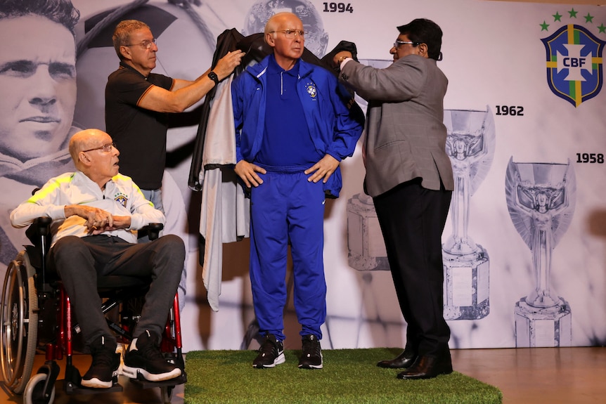 Mário Zagallo sits in a wheelchair as officials unveil a statue of him in his coaching days at a press conference