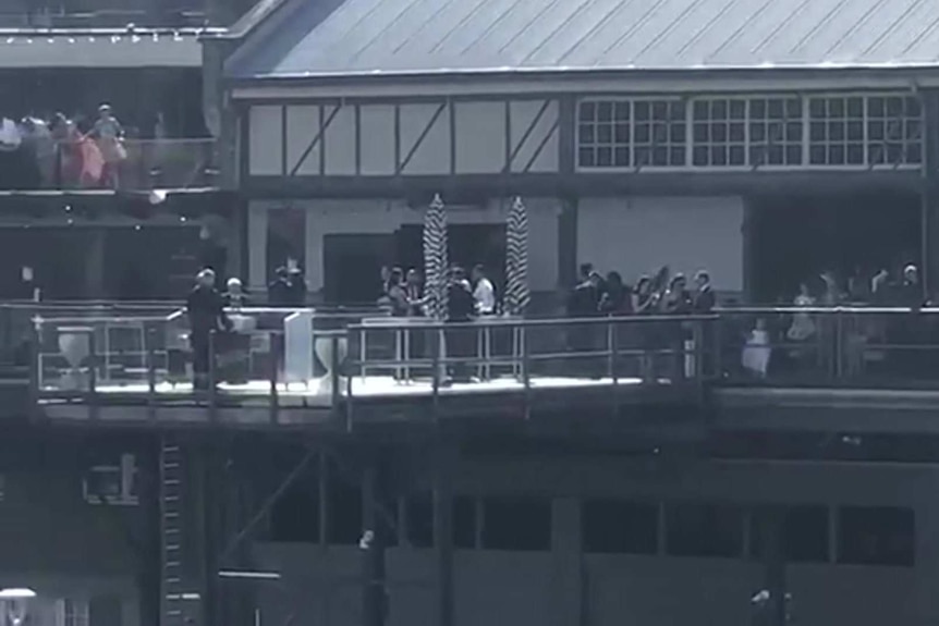 people gathered on the balcony of a venue next to a wharf