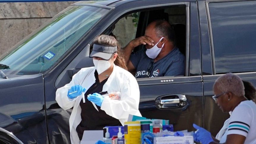 A healthcare worker collects a sample from a man sitting in a car and wearing a mask.