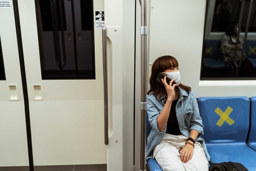 A woman wearing a face mask and talking on a mobile on a train.