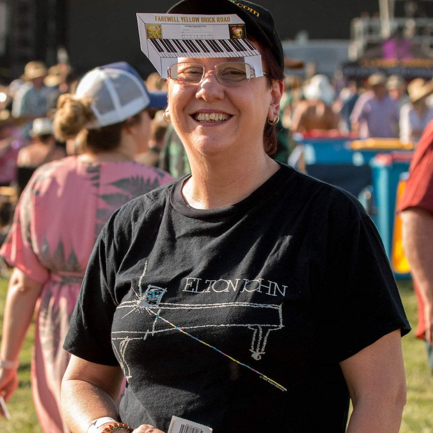 Woman looks at camera wearing a black Elton John fan t-shirt and glasses.