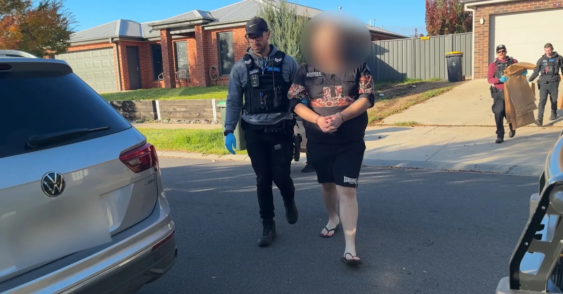 Police officer walking beside a man in handcuffs.