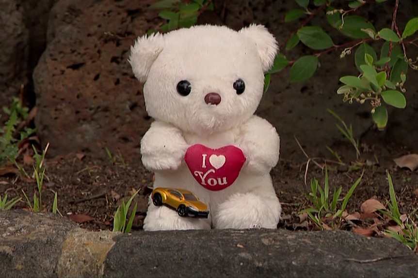 A teddy bear and a toy car left on a rock.