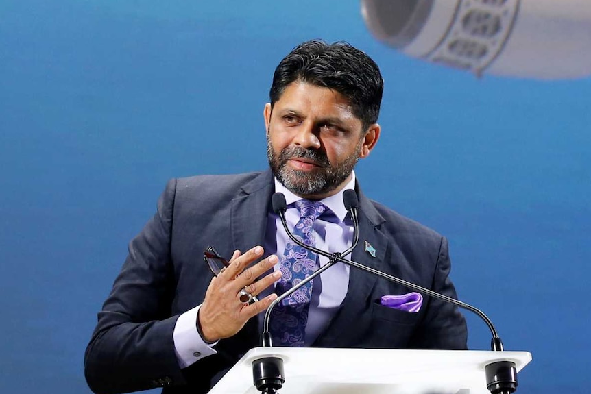 Aiyaz Sayed-Khaiyum stands in front of a large image of a Fiji Airways jet.