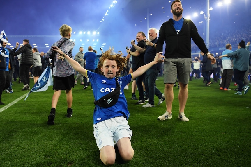 Soccer fans run onto the pitch to celebrate after an important win kept them in the top competition