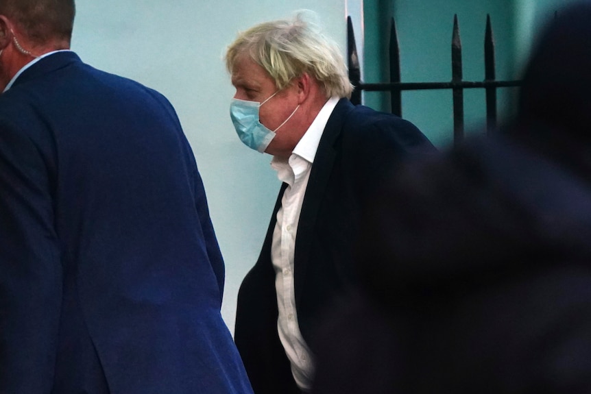 Boris Johnson wearing a mask and navy suit walks into a hospital.