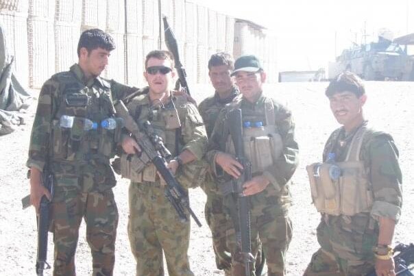 A group of soldiers stand with Phillip Thompson wearing sunglasses and holding a gun 
