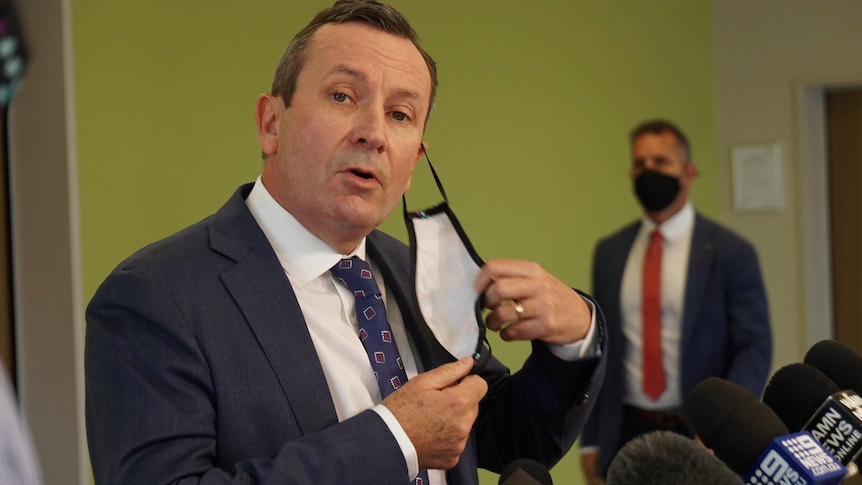 A mid shot of WA Premier Mark McGowan removing a face mask for a media conference indoors.