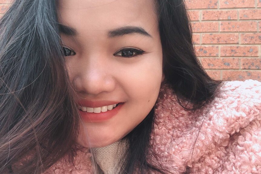 A selfie of a girl with dark hair wearing a pink coat.