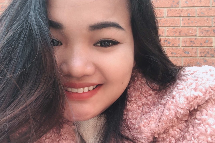 A selfie of a girl with dark hair wearing a pink coat.