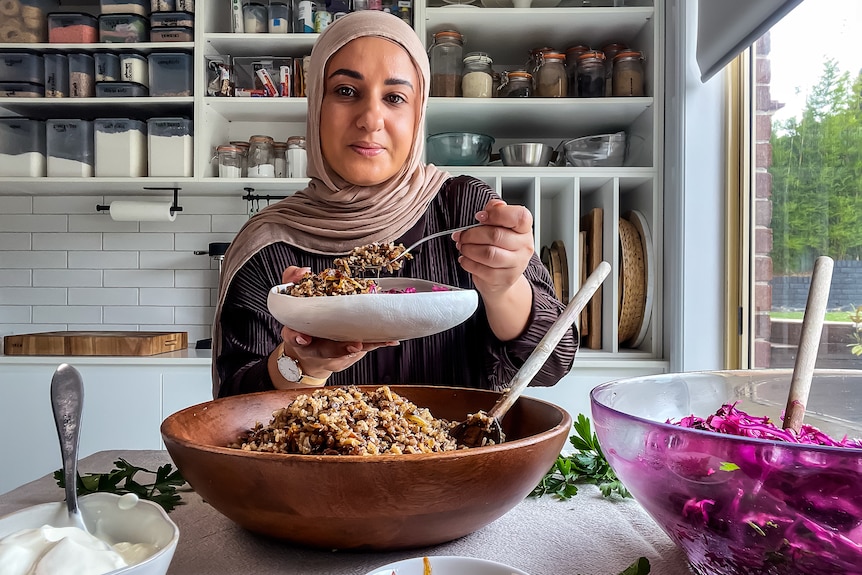 Lina Jebeile in her white kitchen holding a bowl of Mujadarat Roz before the dish ingredients.