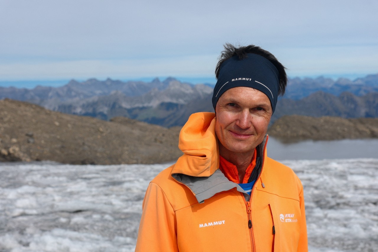 A man smiles at the camera. He is standing on a glacier.