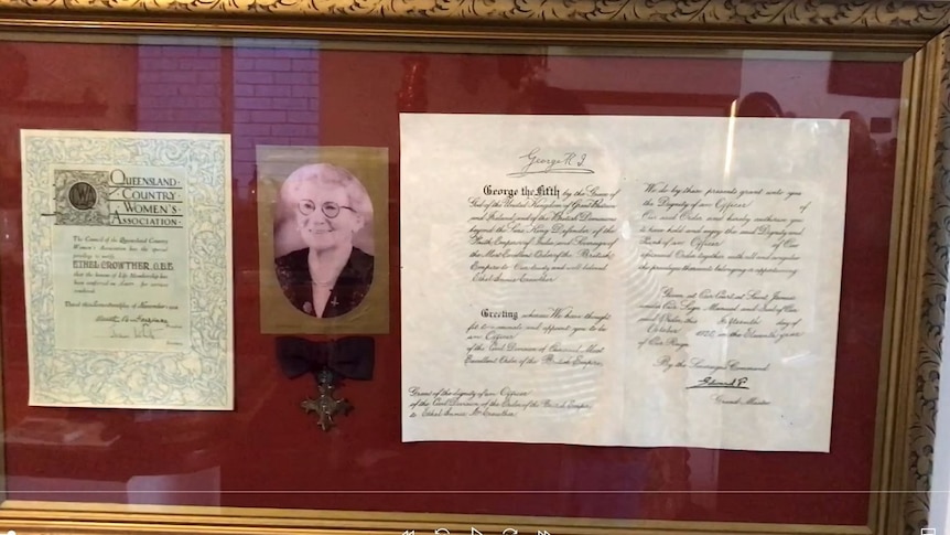 An OBE medal and a photo of an older woman in a frame.