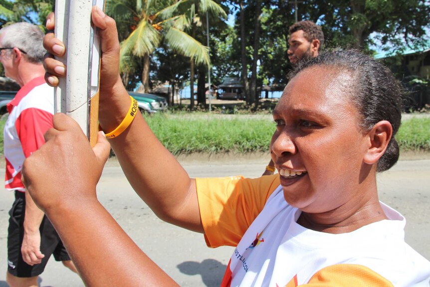 A woman proudly holds the Queens Baton high in front of her face as she runs down the road.