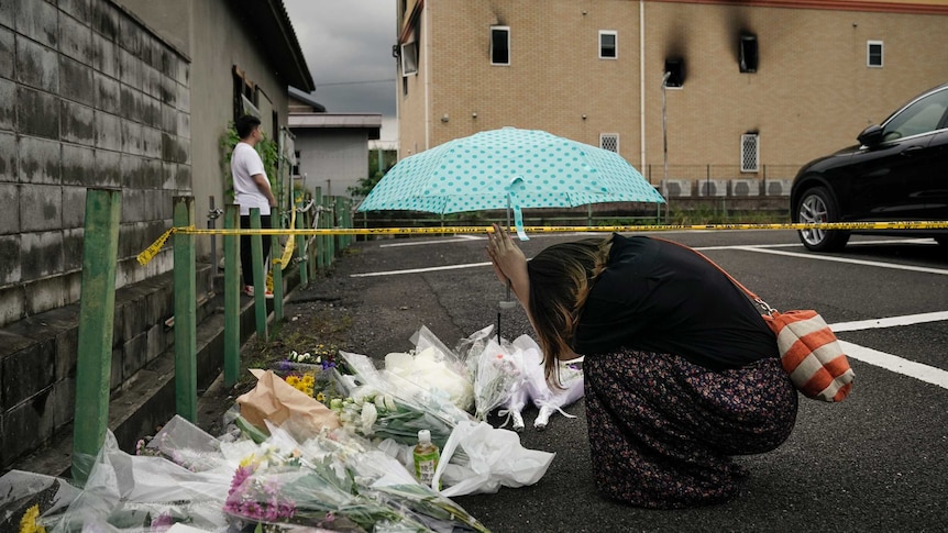 A woman kneels down and prays in front of flowers at the animation studio