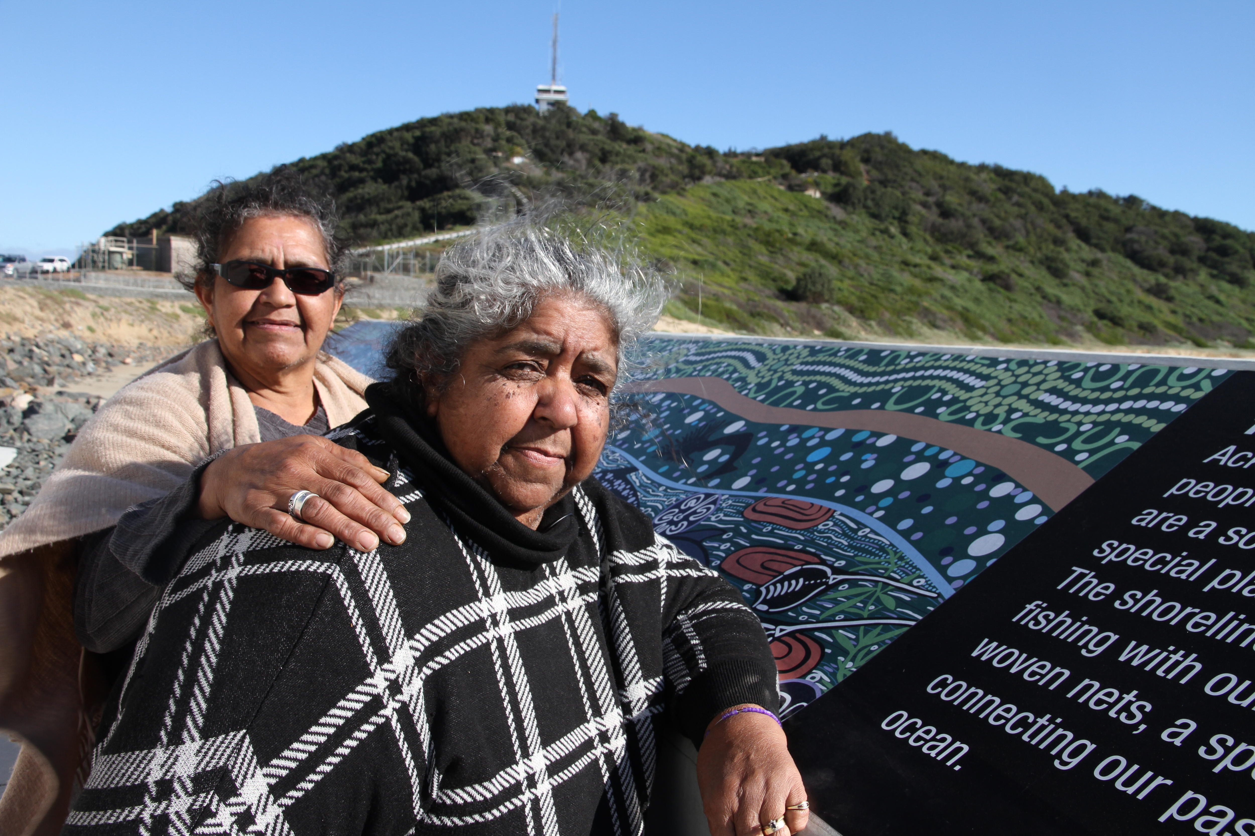 Duas mulheres estão num cais ao lado de uma obra de arte pública. 