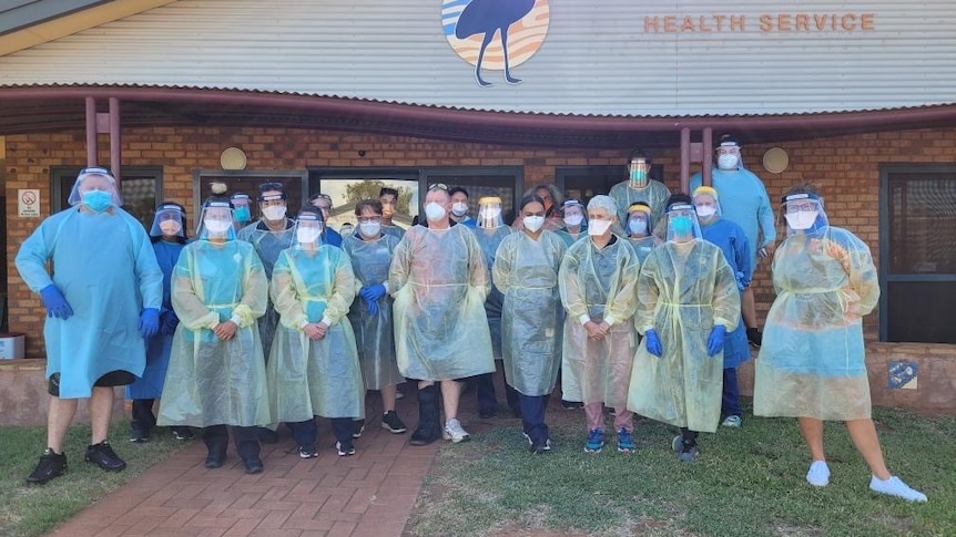 A group of health professionals stand outside a clinic wearing personal protective equipment