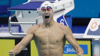 Swimmer Sun Yang celebrates while sitting on a lane rope in a pool.