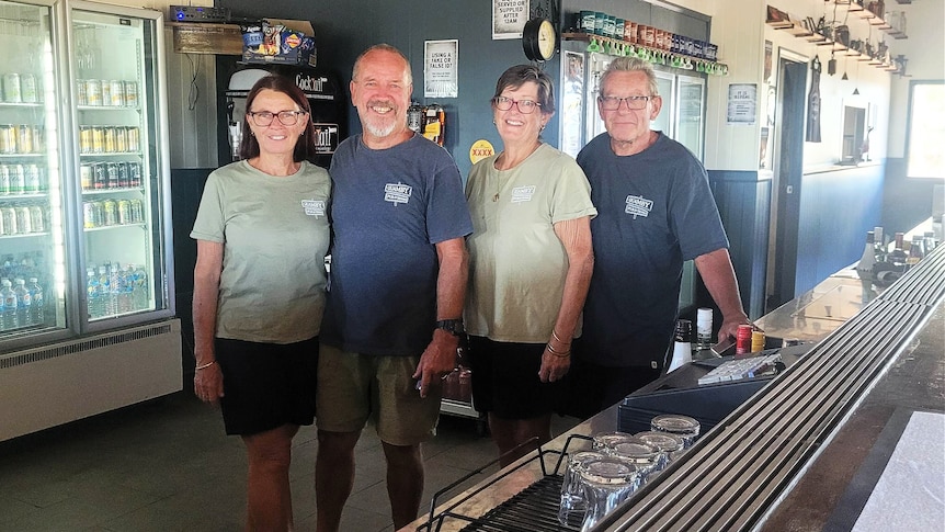 Two women and two men in casual t-shirts stand inside a country pub smiling