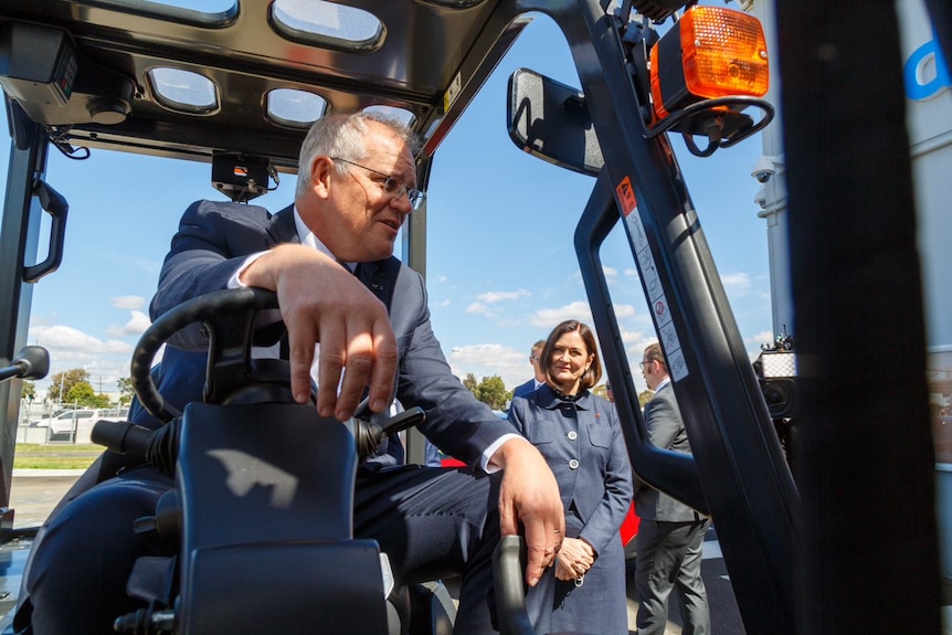 A man sits in the cab of a tractor wearing a suit. 