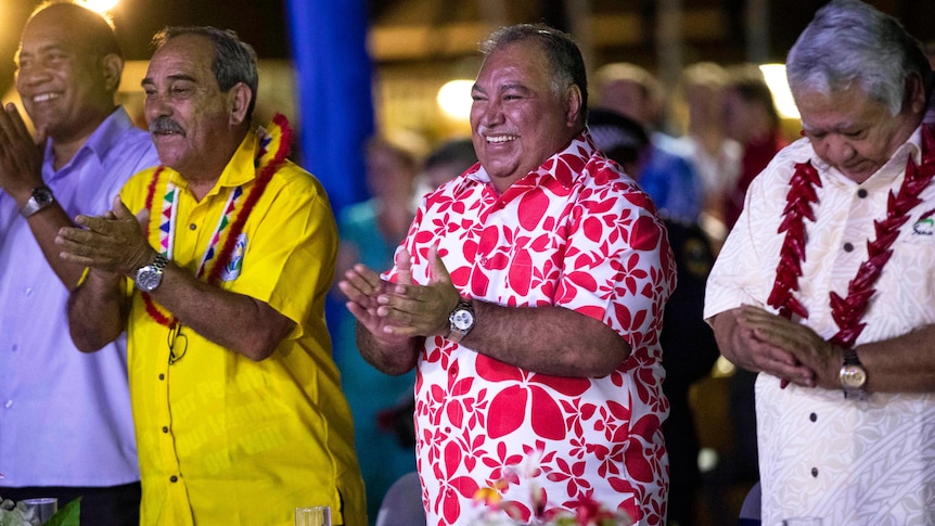 Baron Waqa in a colourful shirt clapping his hands in a line with other men. 
