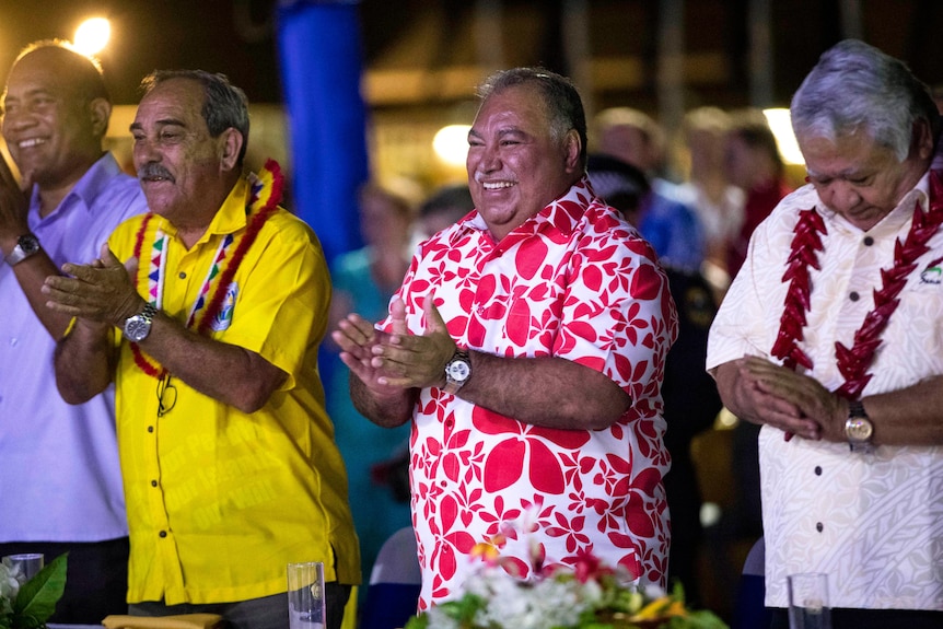 Baron Waqa in a colourful shirt clapping his hands in a line with other men. 