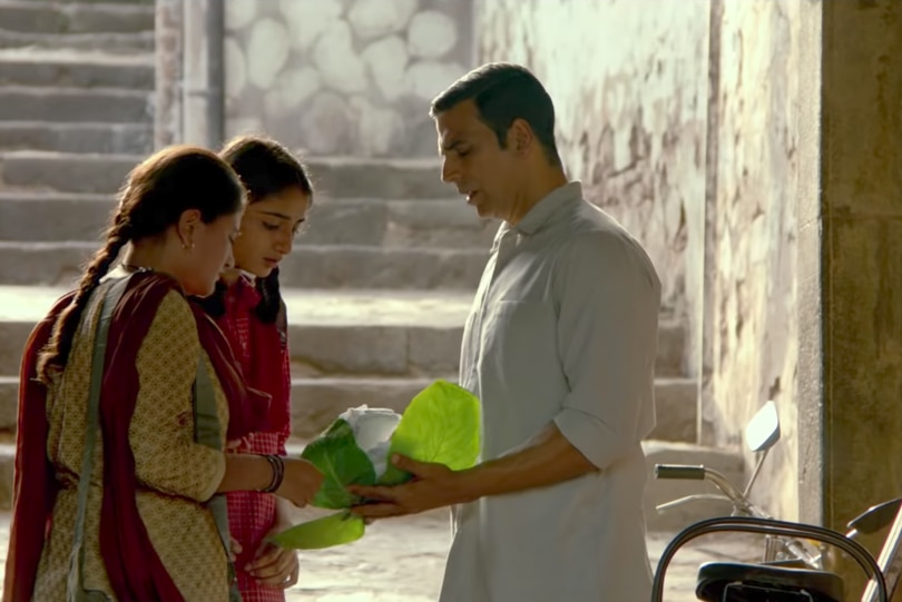 Two women look at sanitary pads sitting in green leaves held by a man.