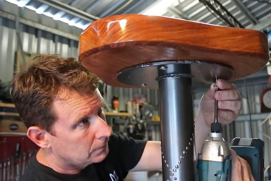 Scott Turner drills a wooden seat onto a bar stool base.