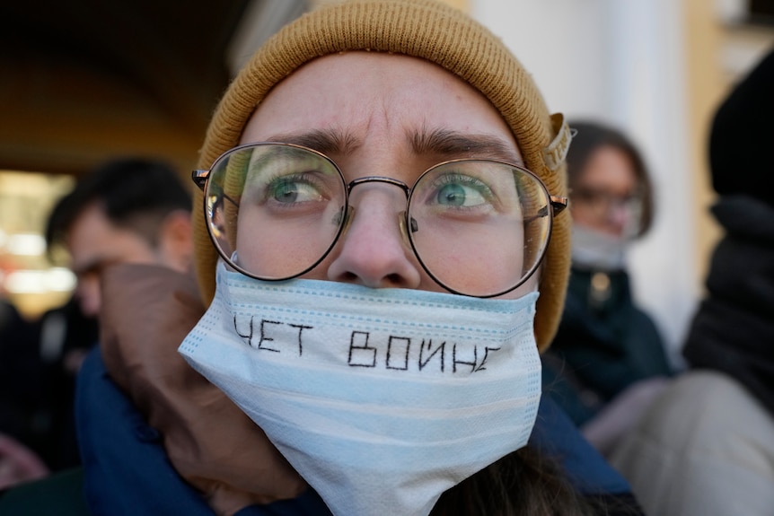 A woman wears a mask that has "no war" written on it in Russian
